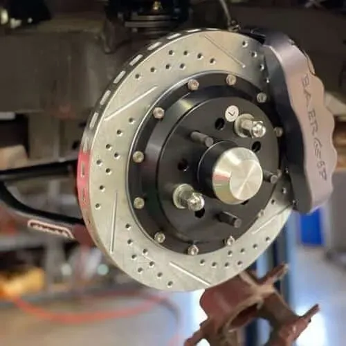 A high-performance Baer disc brake kit with a cross-drilled and slotted rotor installed on a vehicle's suspension.