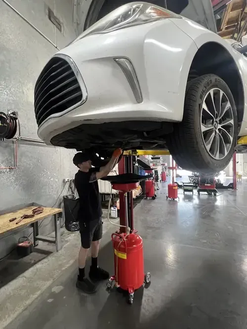 Mechanic working under a white car lifted on a red hydraulic jack in a garage