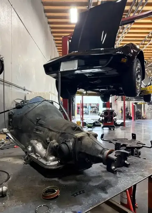 Car on lift in auto shop with a large transmission or engine assembly on the floor beneath it