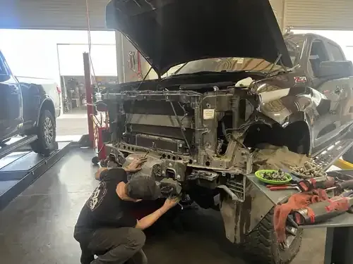 Mechanic inspecting a wrecked black SUV in an auto repair shop, front end disassembled.