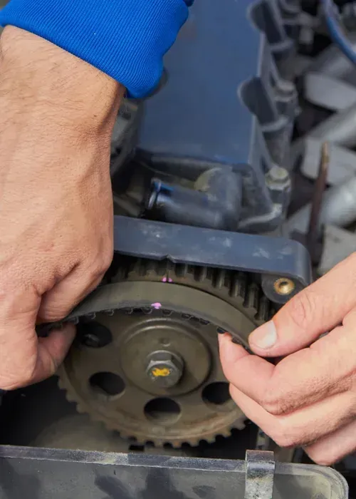 Hands adjusting a car engine timing belt and gear assembly close-up