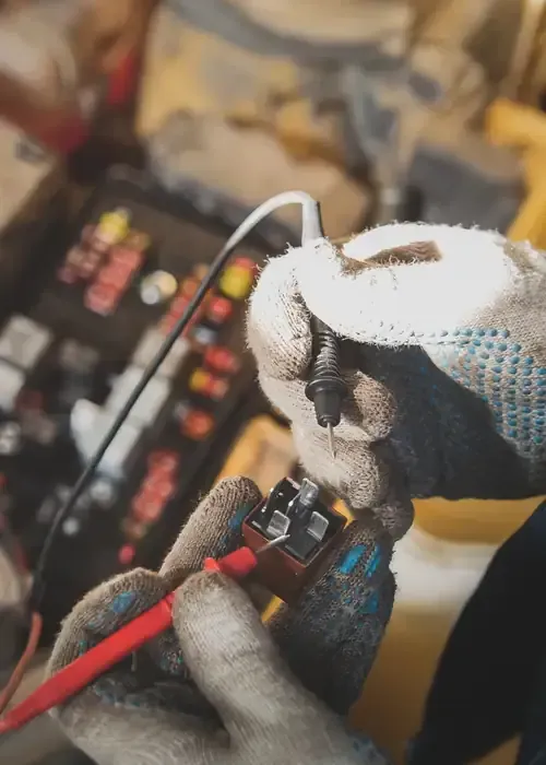 Gloved hands using jumper cables on a car battery in a vehicle engine compartment