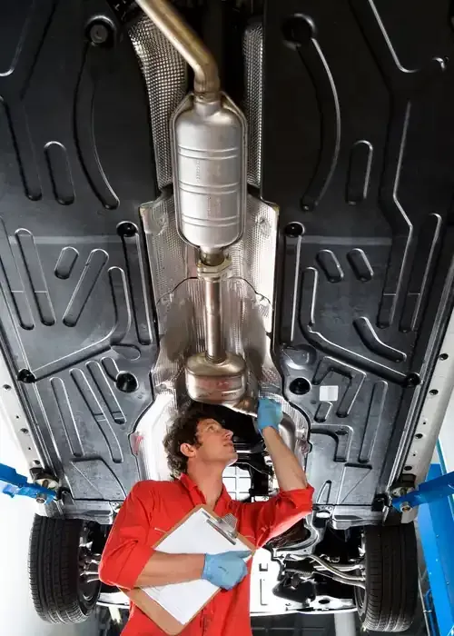 Mechanic inspecting exhaust system under a car on a lift, wearing red coveralls and blue gloves