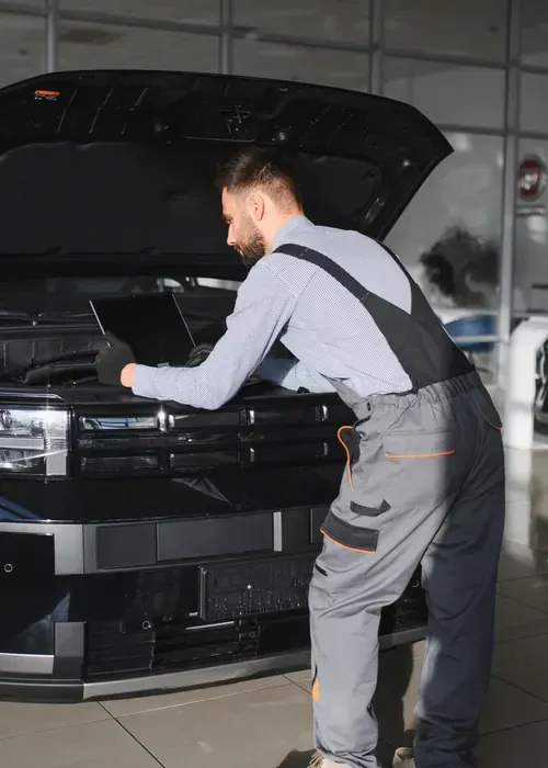 Mechanic inspecting the front of a black car in an auto shop with the hood open