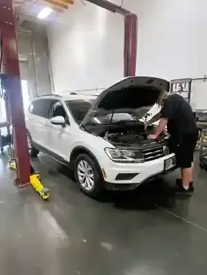 White SUV in an auto repair shop with the hood open while a mechanic inspects the engine.