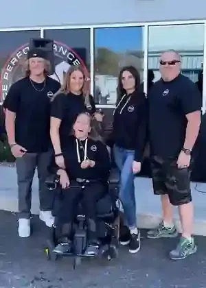 Five people posing outside a storefront, including one person seated in a motorized wheelchair.