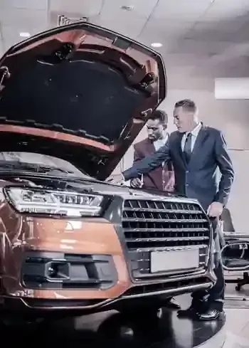 Two men inspecting a bronze SUV with its hood open in a showroom