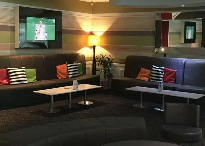 Lounge Area With Dark Sofas, Small Tables, and a Tv Screen — Capricorn Tavern in Taranganba, QLD