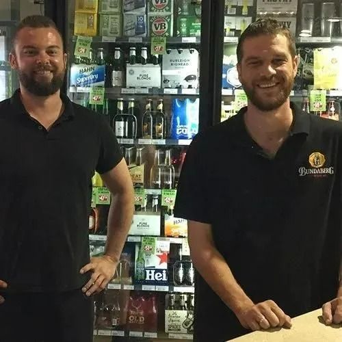 Two Men in Black Shirts Smile at a Store Counter in Front of a Cooler of Beverages — Capricorn Tavern in Taranganba, QLD