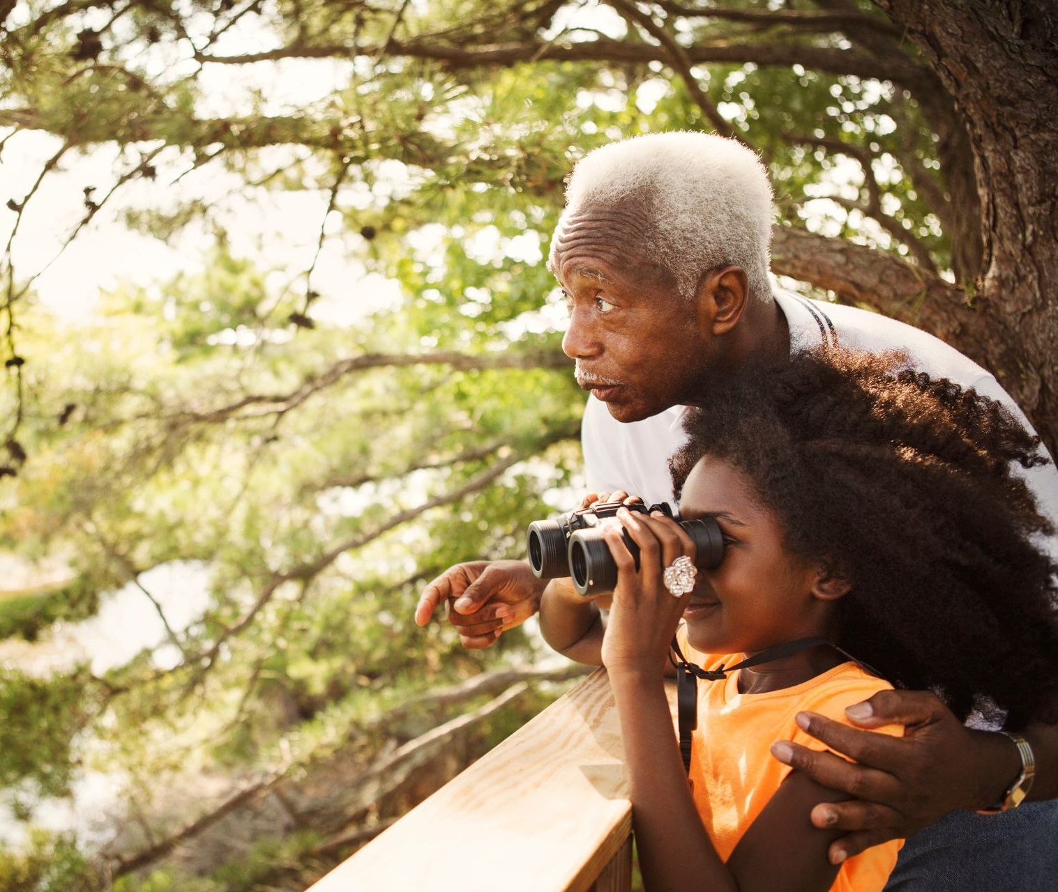 A man and a girl are looking through binoculars at a lake.