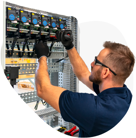 Technician adjusting wiring in an electrical control panel with tools, wearing gloves and safety glasses.