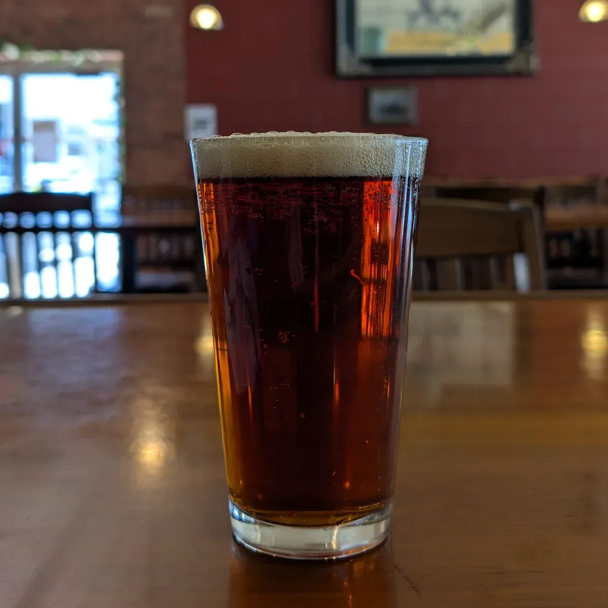 Pint glass of dark beer on a wooden table in a restaurant, with a blurred bar in the background