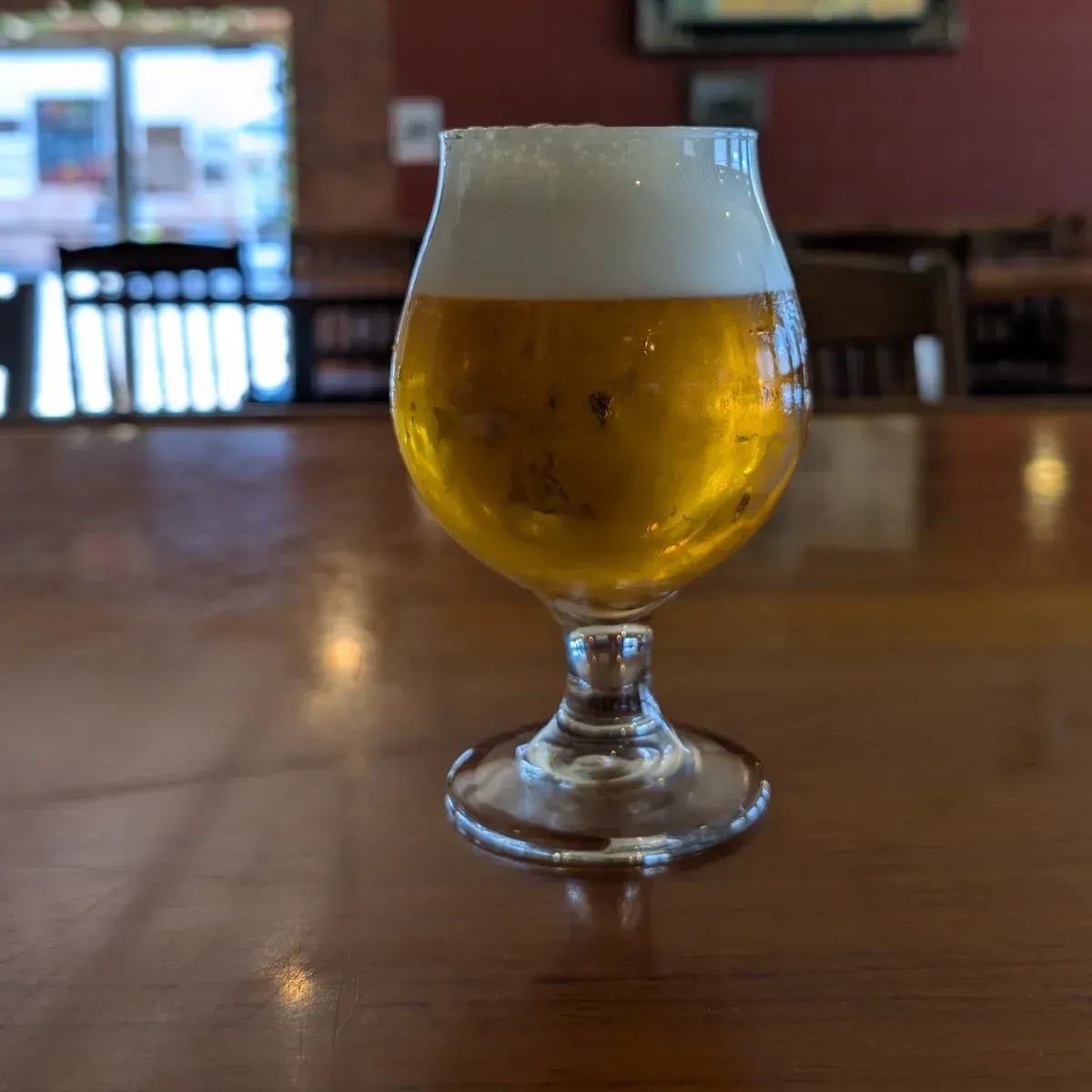 Pint of golden beer with a foamy head on a wooden table in a dim bar