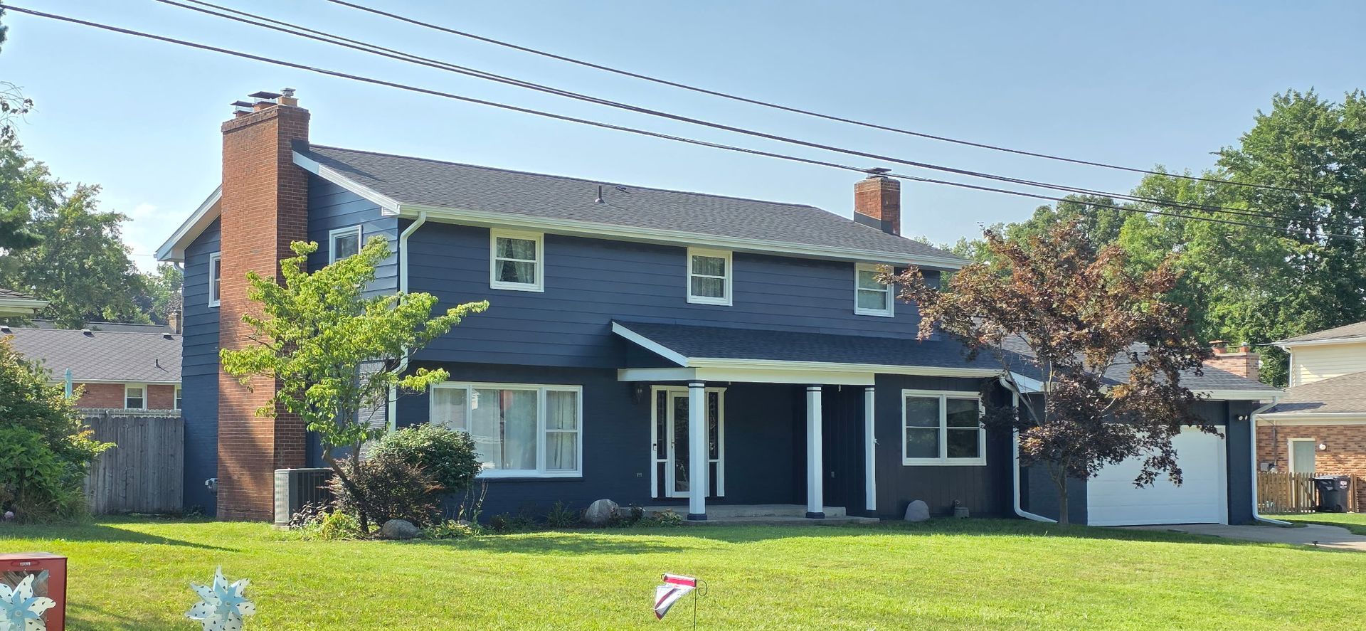 Blue two-story house with white trim, brick chimney, and a green lawn under a clear sky