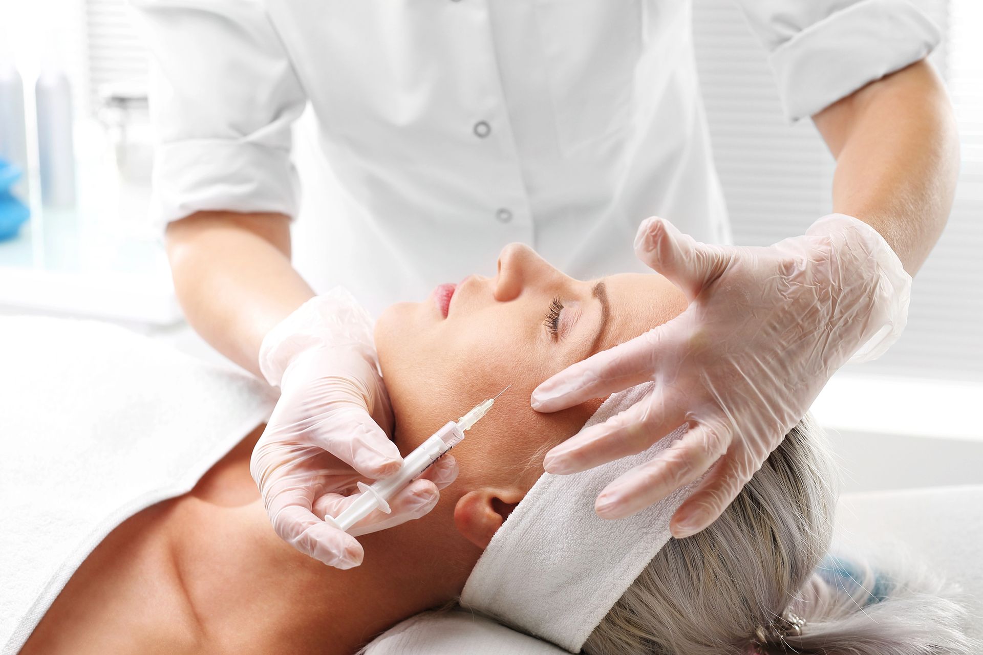 Persona recibiendo una inyección facial de un profesional médico. Ropa y guantes blancos.