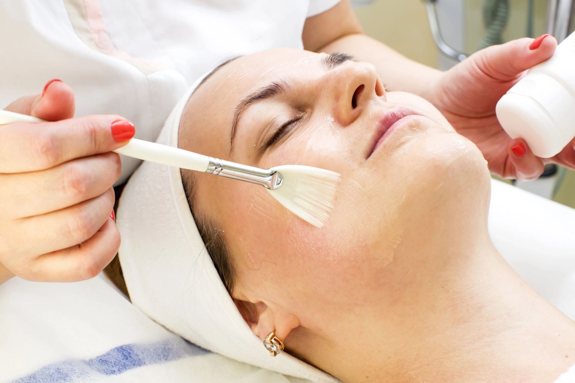 Tratamiento facial: Se aplica un producto en el rostro, con los ojos cerrados. Se coloca un paño blanco en la cabeza. El ambiente es de spa.