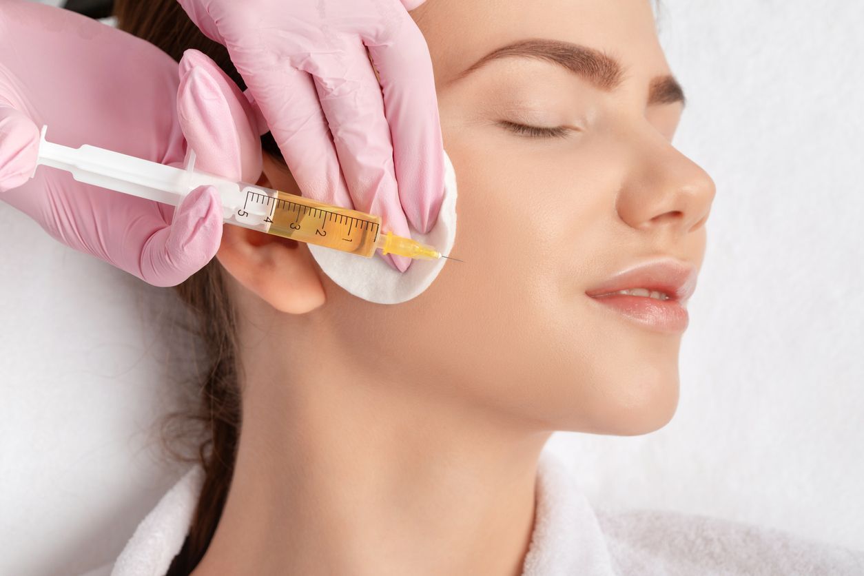 Mujer recibe una inyección facial con una jeringa, sostenida por manos enguantadas, en un spa.