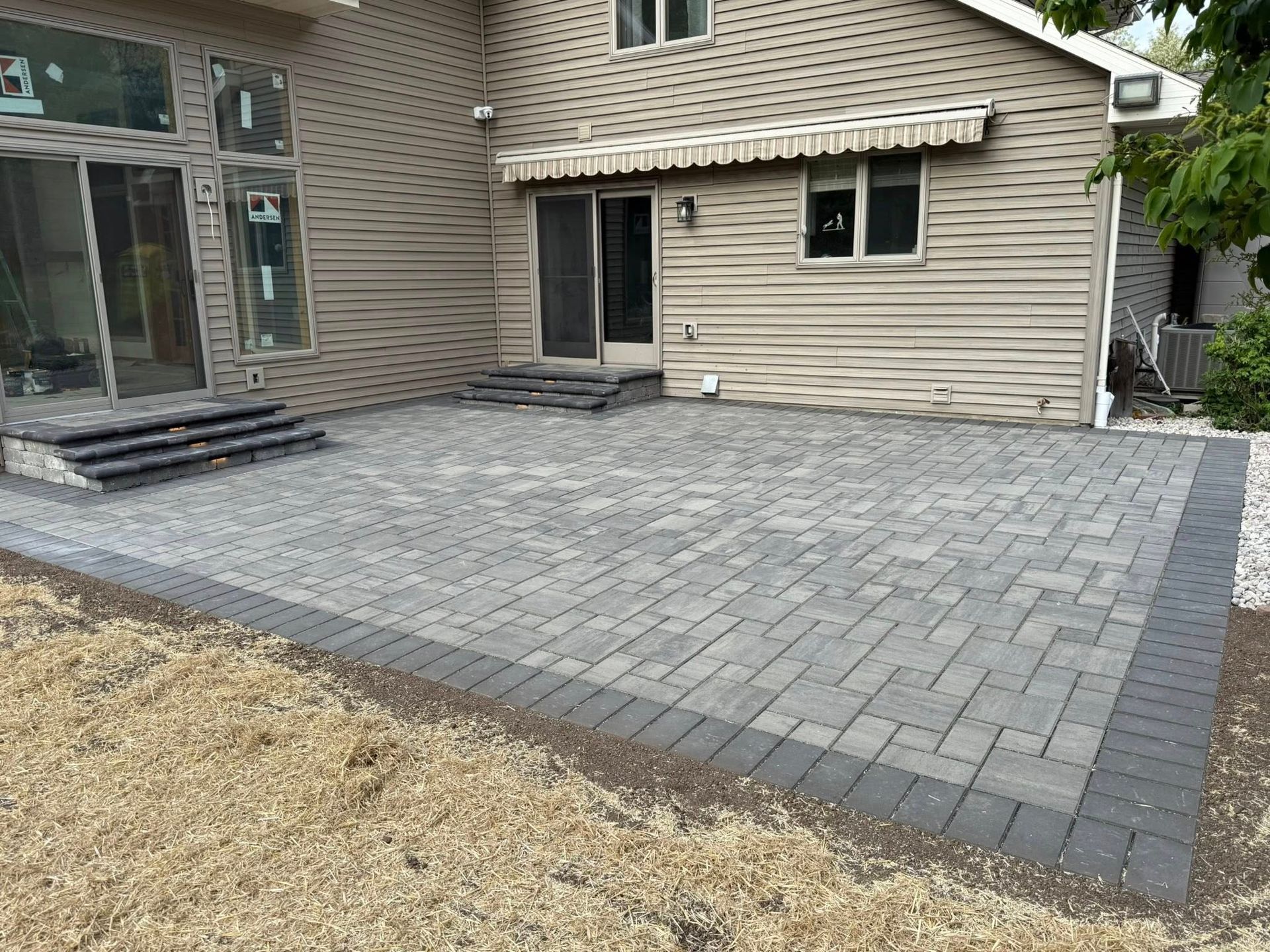 Paver patio in front of a beige house with sliding glass doors and steps.