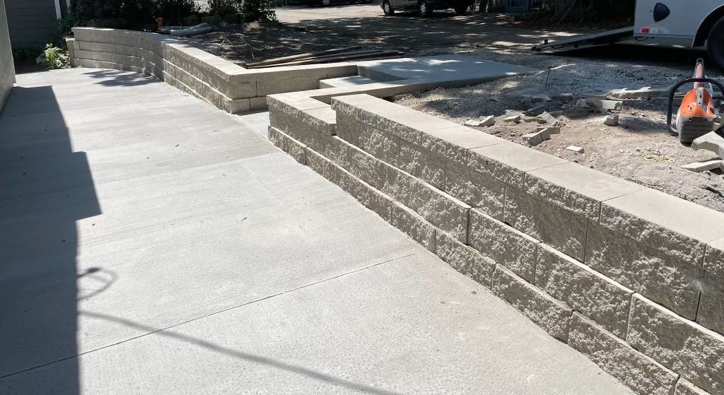 Concrete sidewalk beside raised stone planters in a sunny outdoor area