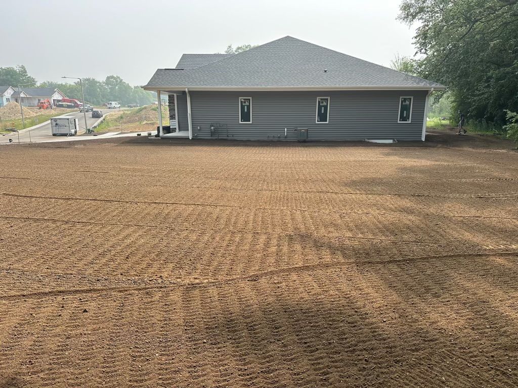 Freshly graded dirt lot with a gray single-story house in the background