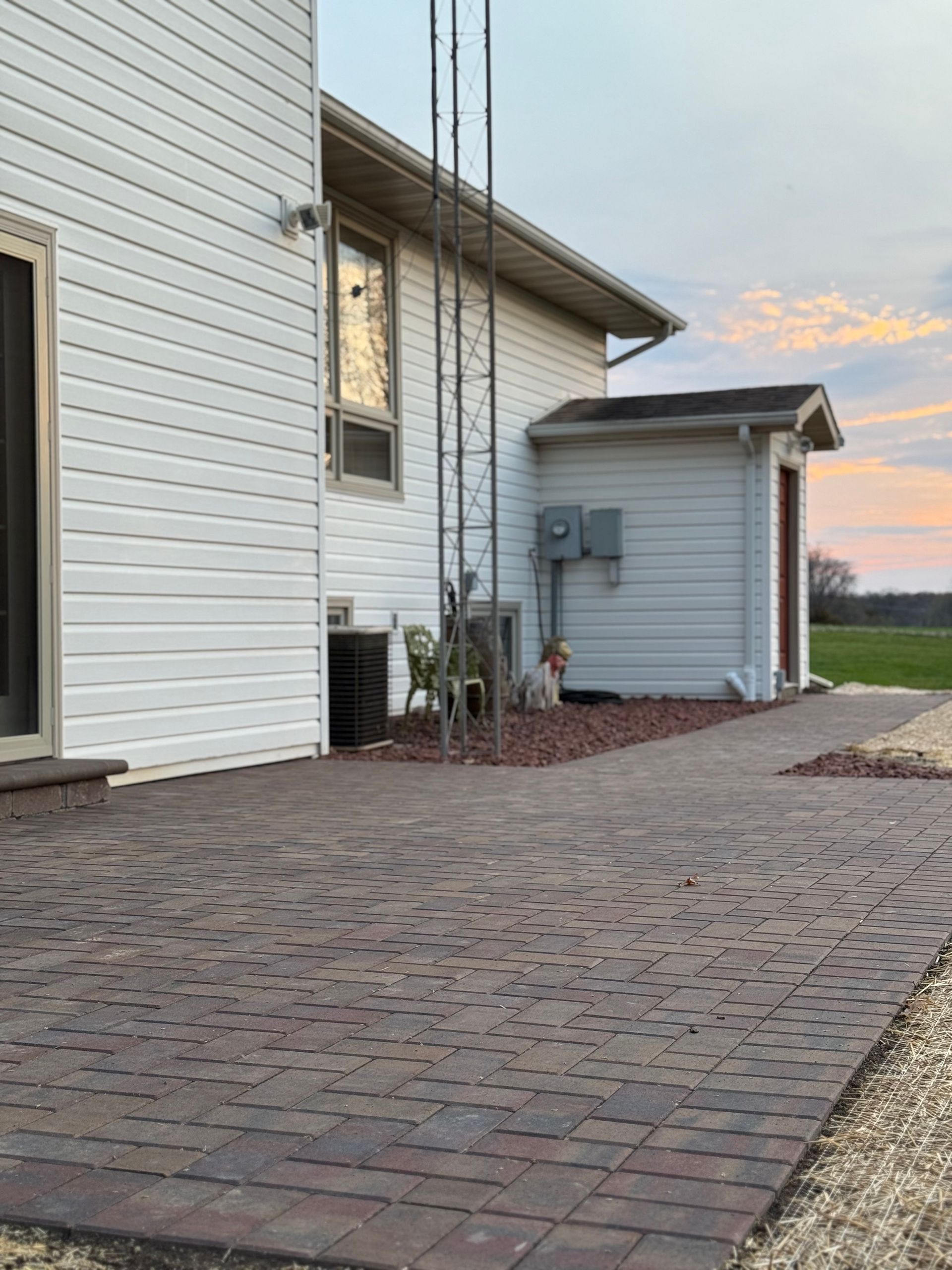 Brick-paved patio beside a white house at sunset