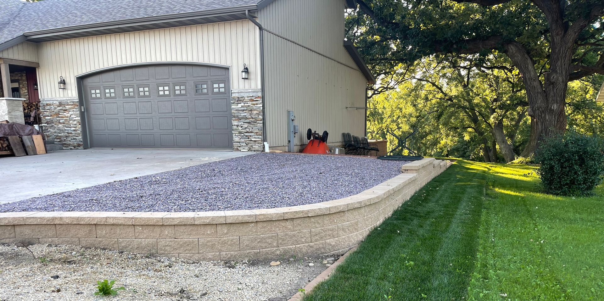 Detached garage with gravel driveway, concrete ramp, and green lawn beside trees