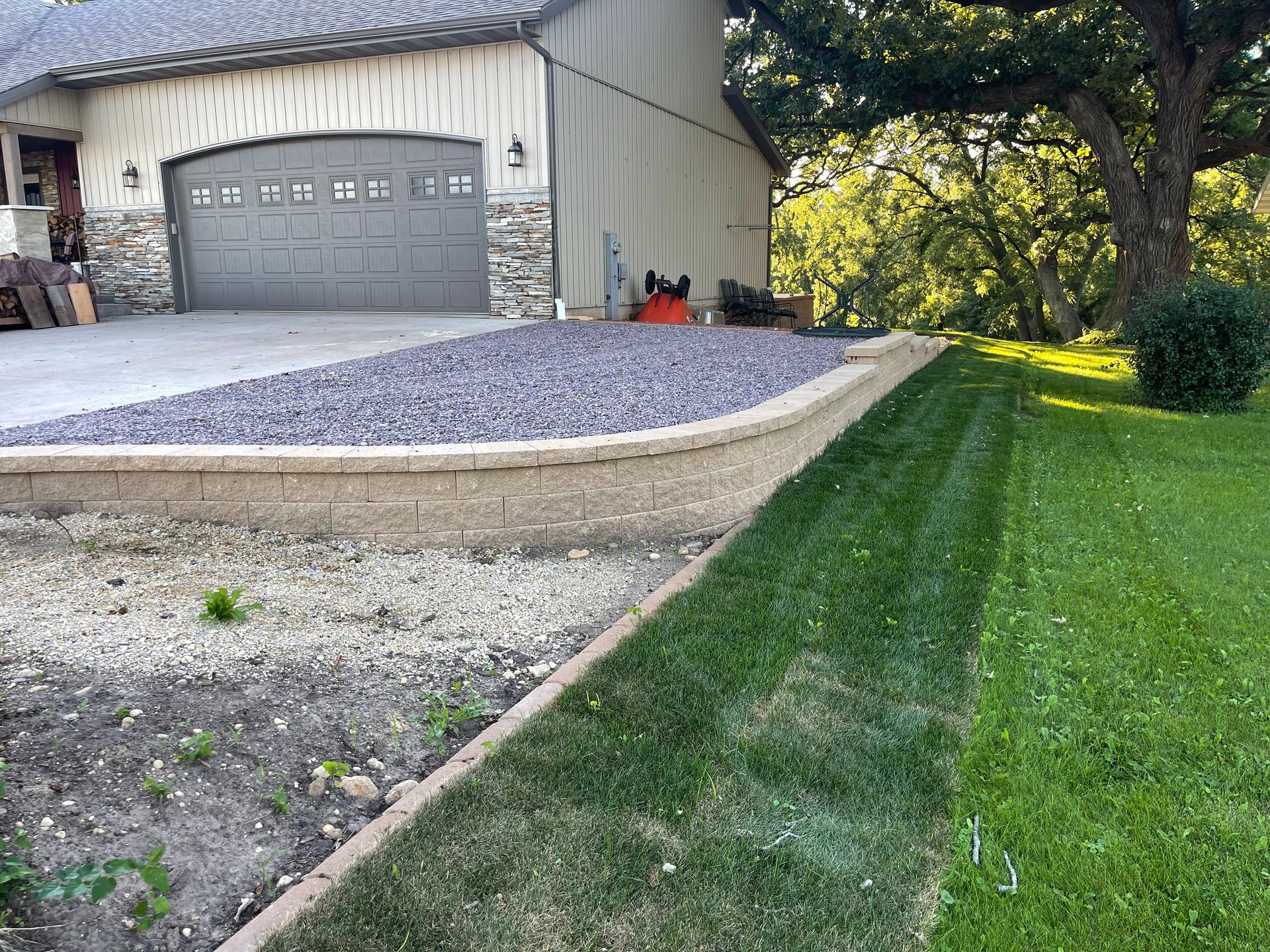 Gravel driveway beside a garage, bordered by a grassy lawn and shaded trees.