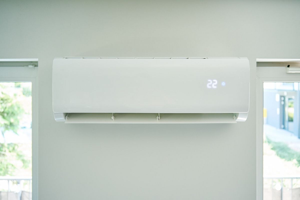 A person in a white shirt opening the plastic front panel of a wall-mounted air conditioner to inspect its filter — EcoAir Conditioning in Coconut Grove, NT