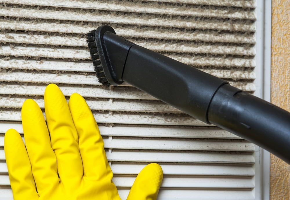 Person Wearing Yellow Gloves Vacuuming a Dirty Air Vent With a Black Nozzle — EcoAir Conditioning in Coconut Grove, NT
