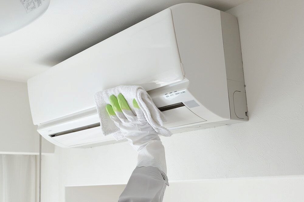 Person in Gloves Wiping a White Air Conditioner on a White Wall With a White Cloth — EcoAir Conditioning in Coconut Grove, NT