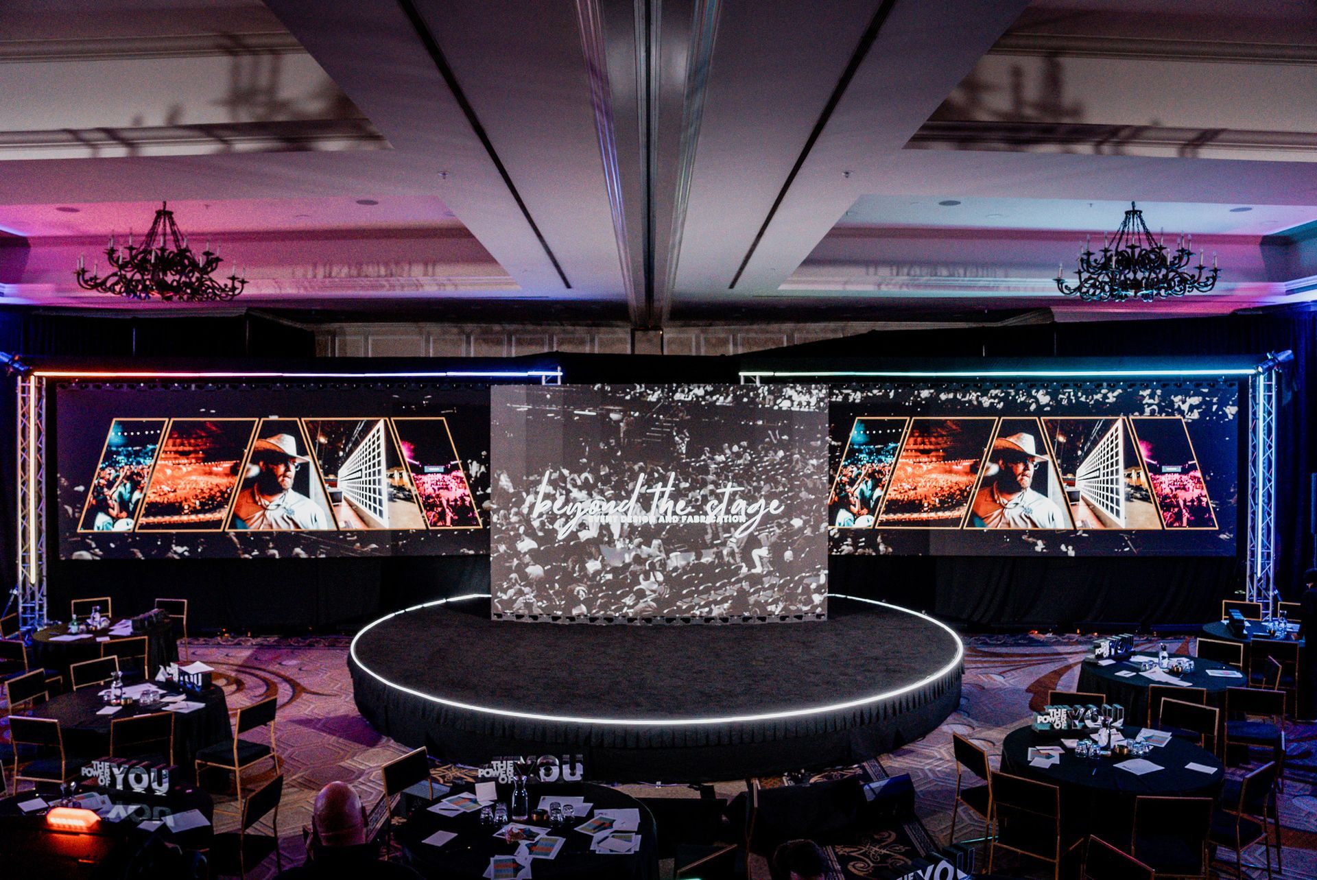 Dimly lit stage with a large central screen and two wide side screens in a nightclub or event venue.