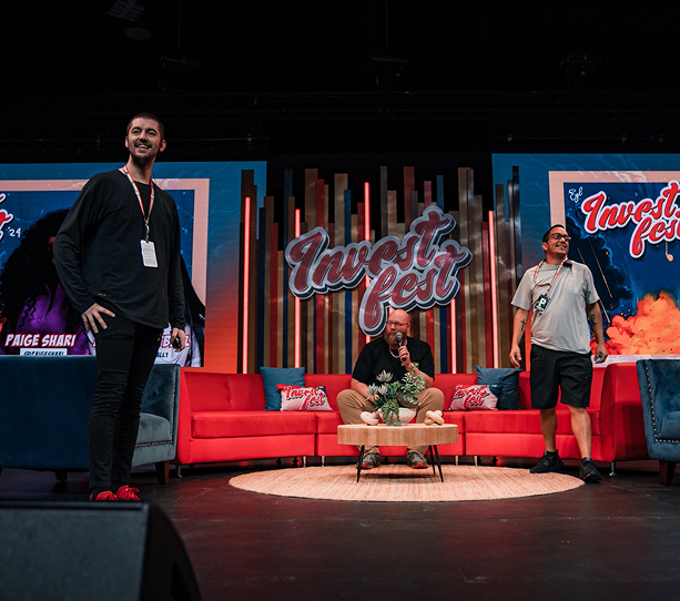 Three people on a stage with red couches and a large “Tremor Fest” sign behind them