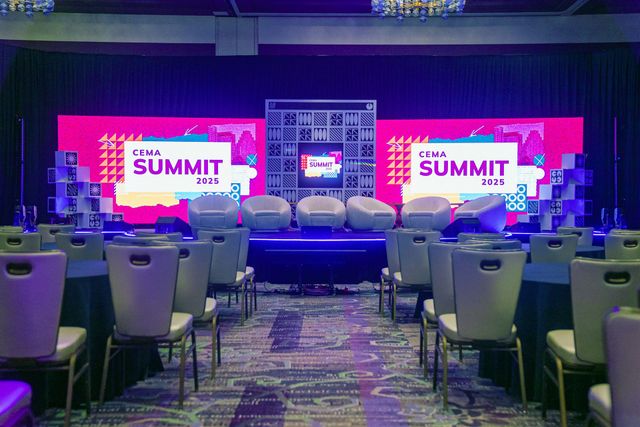 Conference summit stage with pink screens, rows of empty chairs, and a central backdrop in a ballroom.