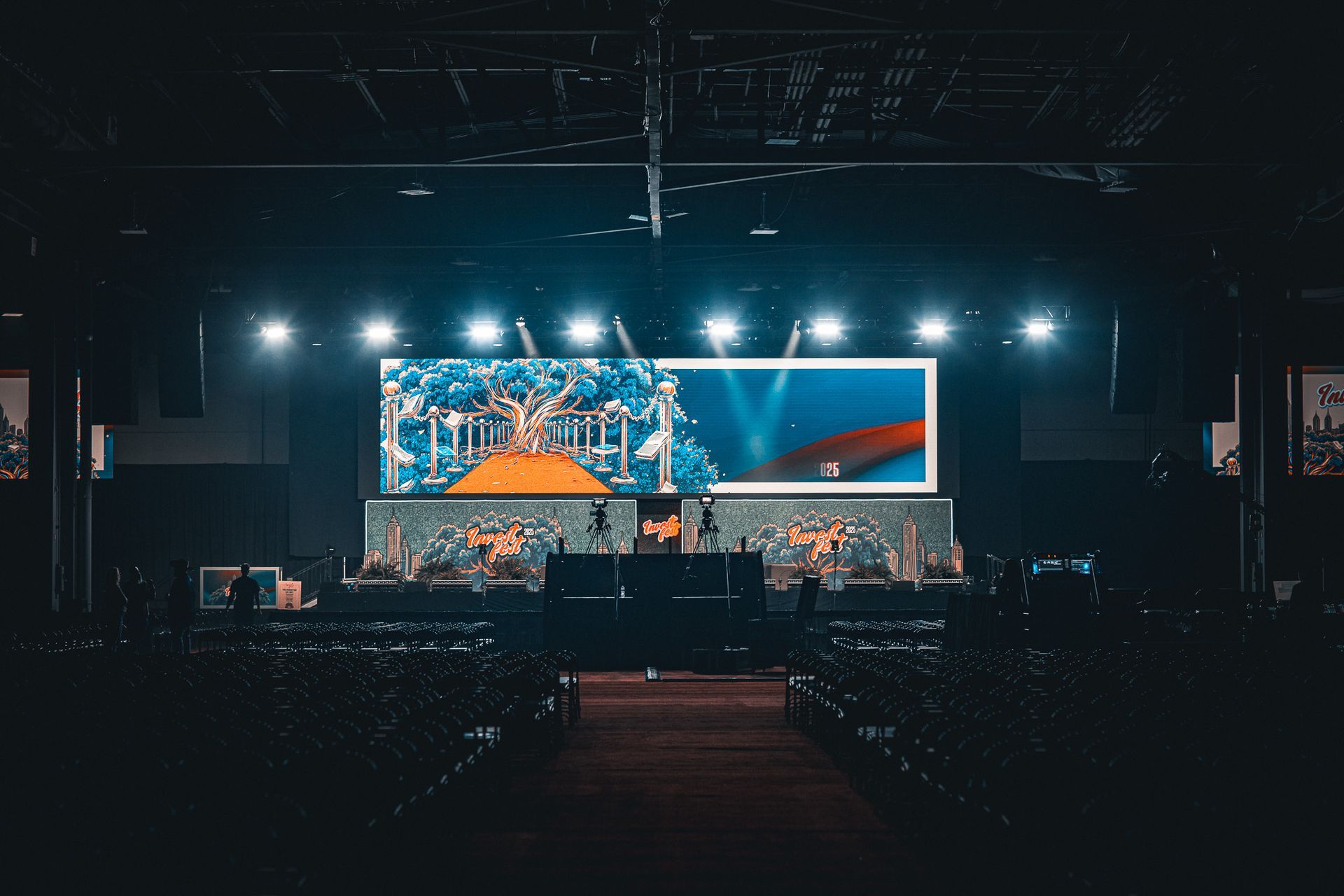 Concert stage with bright blue screen and lights, viewed from a dark audience area