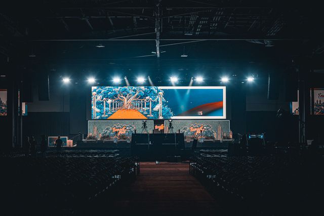 Concert stage with bright lights and large screen, viewed from a dark audience area