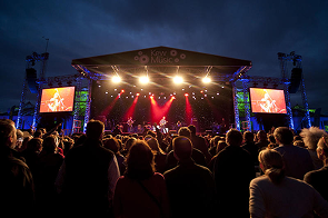 Crowd watching a live concert on an outdoor stage lit with red and yellow lights at night
