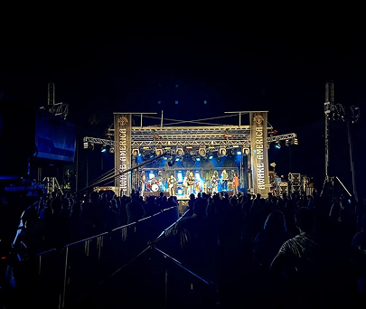 Nighttime outdoor concert with bright blue stage lights and a crowd facing the stage