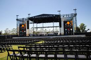 Empty outdoor concert stage with rows of black chairs in front and “Great Park Live” signage overhead