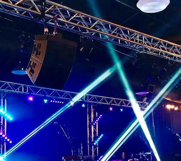 Concert stage with blue and white spotlights crossing beneath a truss rig