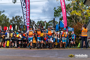 Cyclists lined up at a race start under pink banners beside the road