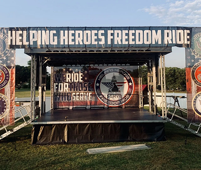 Outdoor stage with “Helping Heroes Freedom Ride” banner and Ride for the Brave event signage