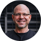 Smiling bald man with glasses in a black shirt against a dark blurred background