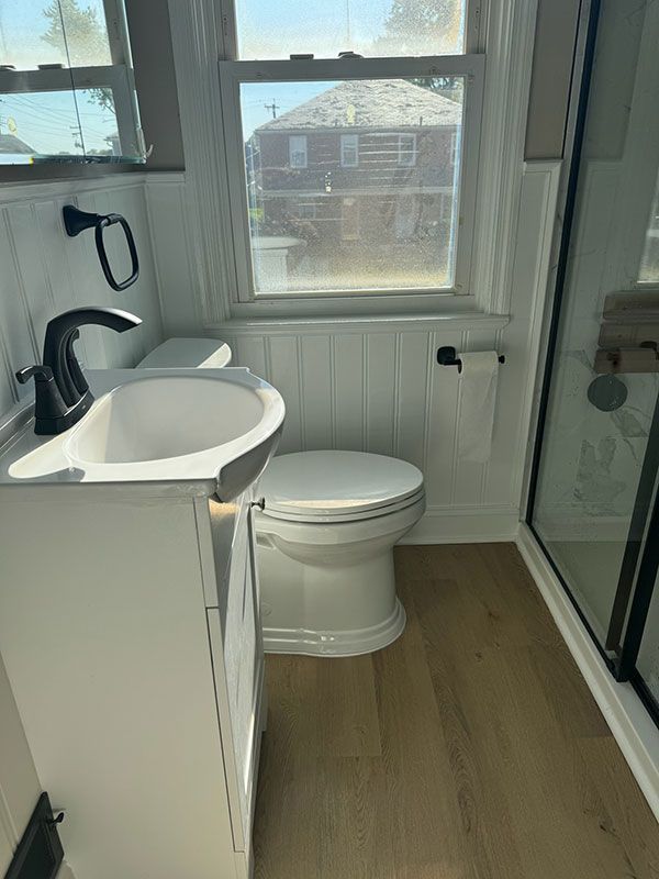 White bathroom with a sink, toilet, and glass shower. Window provides natural light.