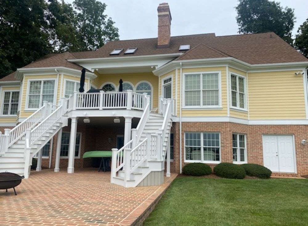Yellow house with white trim, brick patio, and green lawn.