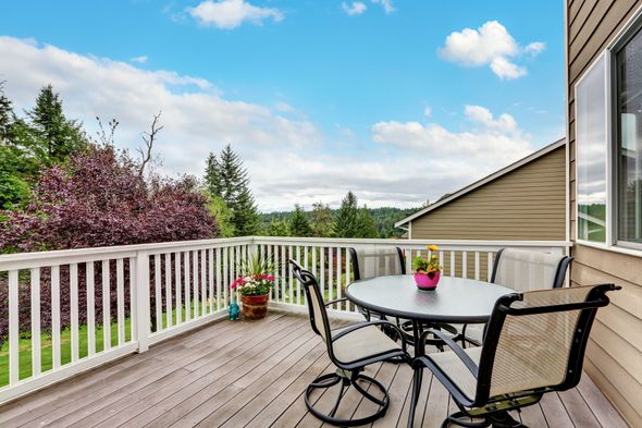 Deck with round table and chairs, overlooking trees and a blue sky.