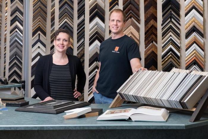 Two people standing behind framed samples and open books in a flooring showroom