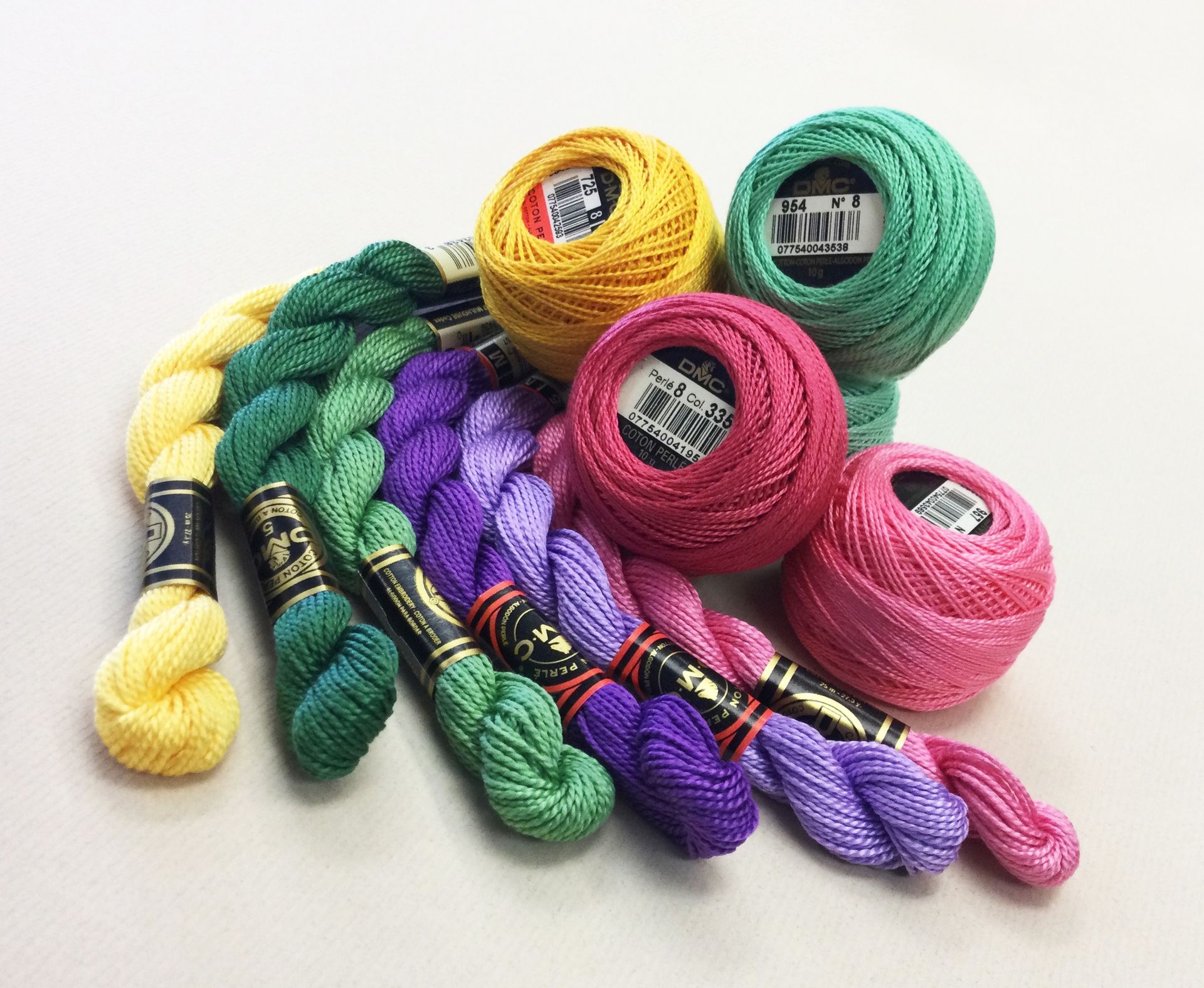 Assorted colorful skeins of embroidery floss and thread arranged on a white background