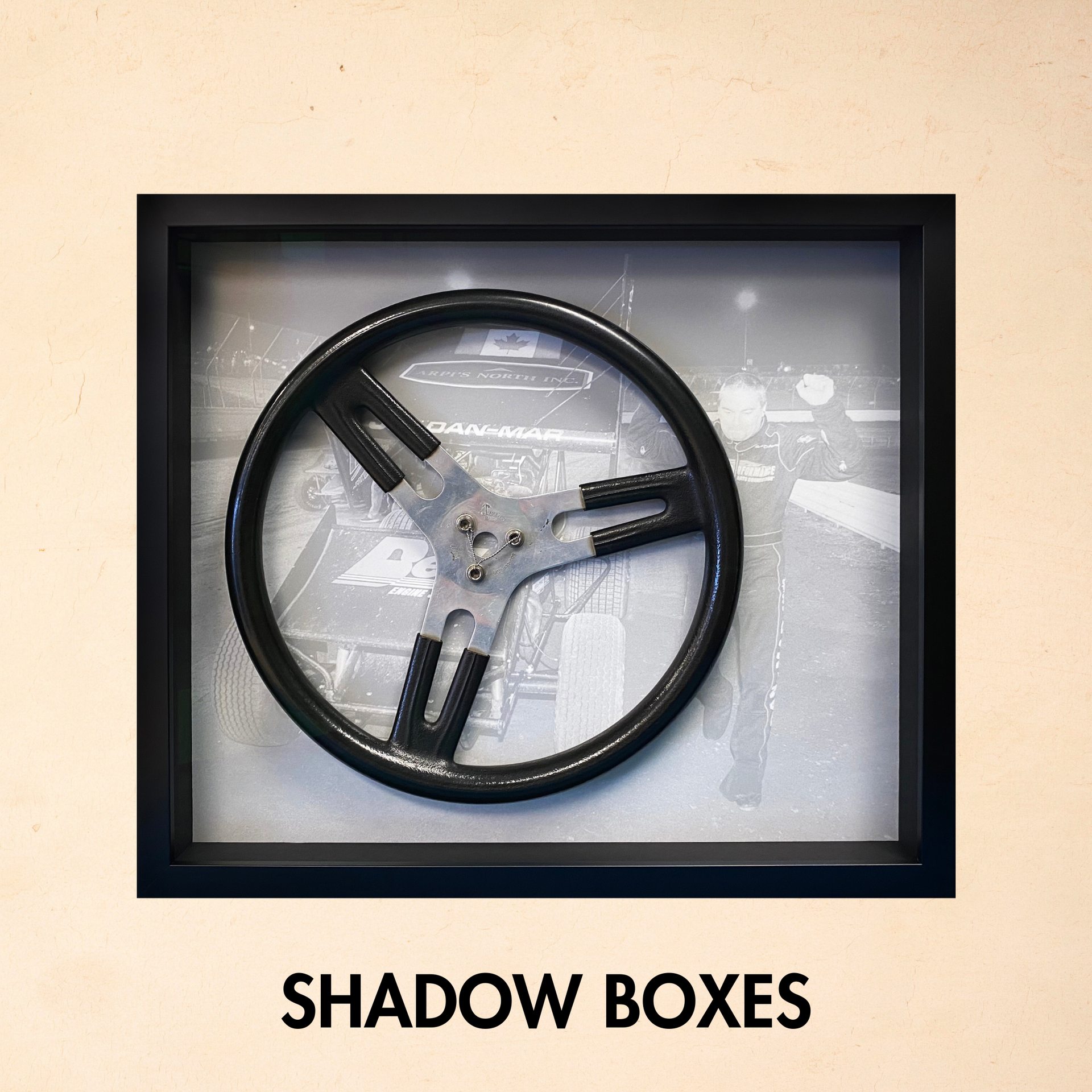 Black-framed shadow box with a circular metal sculpture and the words “SHADOW BOXES” below