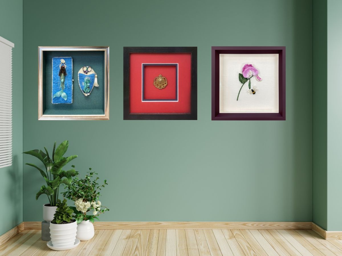 Three framed flower artworks on a green wall above potted plants
