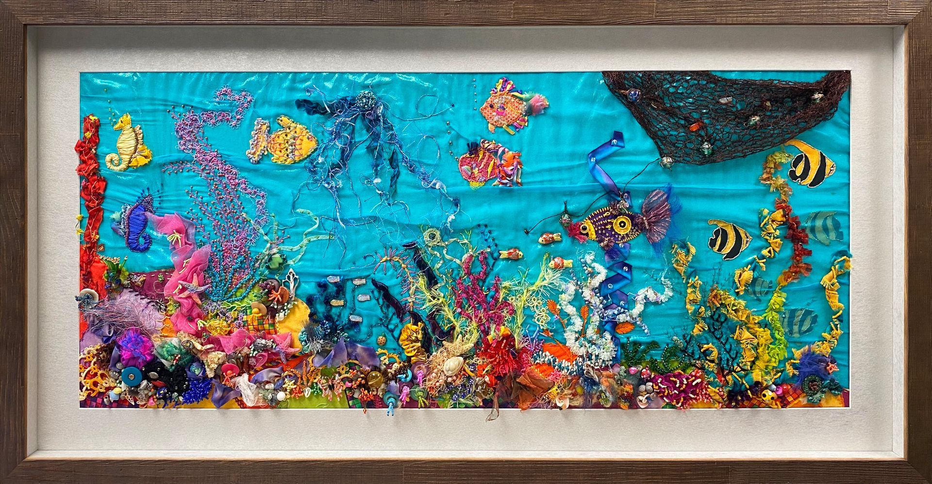 Colourful underwater needlework artwork featuring tropical fish and coral in a dark wooden frame.
